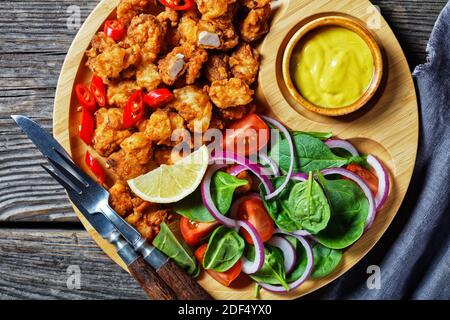 Pollo croccante di popcorn fast food americano servito su un piatto di bambù con senape americana e insalata di spinaci, cipolla rossa, pomodori ciliegini e lem Foto Stock