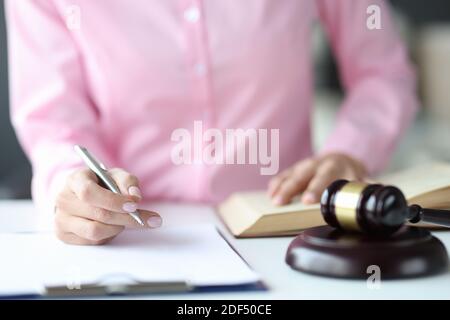 La donna giudica la scrittura nei documenti con la penna a sfera vicino al martello di tribunale Foto Stock