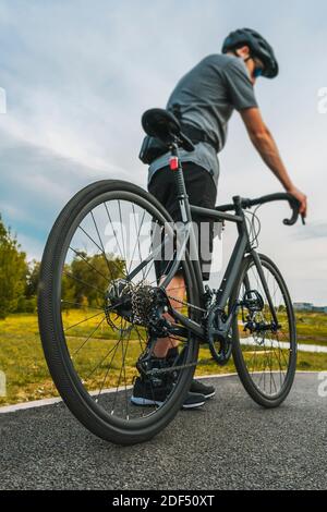 Tiro verticale del ciclista con una bici da strada sulla pista ciclabile asfaltata. Primo piano della ruota posteriore. Foto Stock