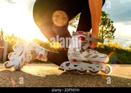 Una donna tensiona i pattini a rotelle sul percorso. Gambe donna con lame a rullo in giornata di sole. Foto Stock