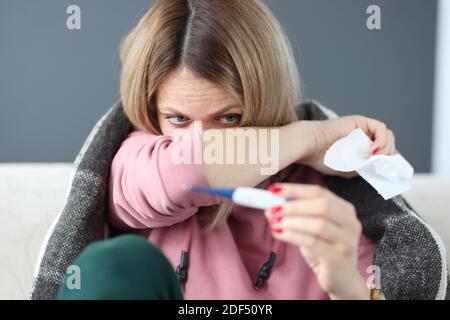 Donna malata che tiene il termometro e tovagliolo di carta sotto le coperture Foto Stock