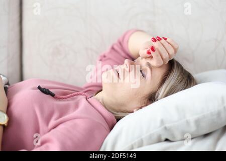 Donna malata sdraiata su divano con occhi chiusi e tenuta la testa Foto Stock