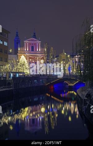 Lubiana, Slovenia - 2 dicembre 2020: Rive innevate del fiume Lubibljanica, ponte triplo, albero di Natale illuminato e Chiesa francescana Foto Stock