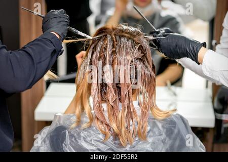 Due delle mani del parrucchiere colorano i capelli femminili con un spazzola in un parrucchiere Foto Stock