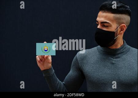 Uomo egiziano in tleneck grigio e maschera di protezione viso nero mostrano Asyut bandiera sfondo isolato. Governatorati di Egitto coronavirus concetto. Foto Stock