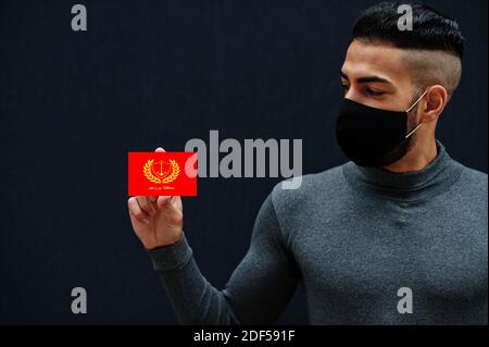 Uomo egiziano in tleneck grigio e maschera di protezione viso nero mostrano Port detto bandiera sfondo isolato. Governatorati di Egitto coronavirus concetto. Foto Stock