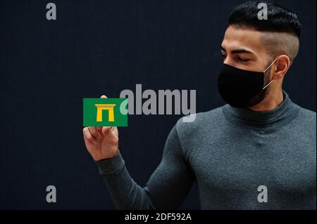 Uomo egiziano in tleneck grigio e maschera di protezione viso nero mostrano Qena bandiera sfondo isolato. Governatorati di Egitto coronavirus concetto. Foto Stock