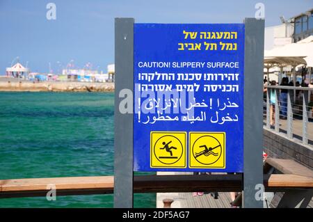 Grande cartello nel vecchio porto di Tel Aviv, avvertimento sul pericolo di scivoloso e proibisce l'ingresso in acqua. Foto Stock