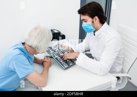 Pulmonologa indossando una maschera chirurgica che mostra ad un paziente anziano una scansione TC dei suoi polmoni. Polmonite, coronavirus, malattie polmonari Foto Stock