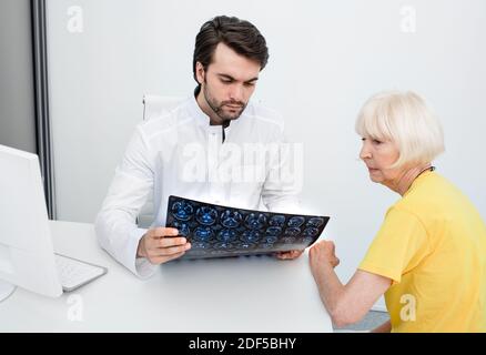 Medico che analizza i risultati MRI cervello di una donna anziana. Diagnosi di malattie e lesioni alla testa. Trattamento del mal di testa Foto Stock