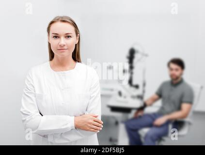 Ritratto di una bella donna oftalmologista in un moderno ufficio oftalmologico, sullo sfondo un bel paziente maschile è seduto Foto Stock