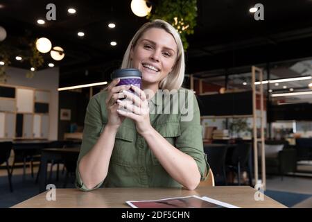 Ritratto di felice donna d'affari caucasica in ufficio creativo, tenendo una tazza di caffè Foto Stock