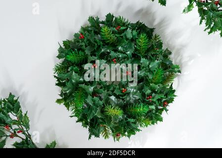 Foto di agrifoglio con bacche rosse disposte in una cornice di corona su uno sfondo bianco con ombra. Foto Stock