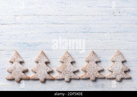 Biscotti al pan di zenzero di farinata d'avena a forma di albero di Natale cosparsi di zucchero in polvere su uno sfondo azzurro, vista dall'alto, spazio libero Foto Stock