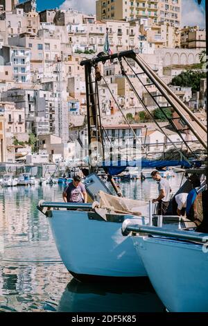 Sciacca Sicilia ottobre 2020, barche da pesca e persone riparano reti nella colorata città di Sciacca che si affaccia sul suo porto. Provincia di Agrigento, Sicilia. Foto di alta qualità Foto Stock