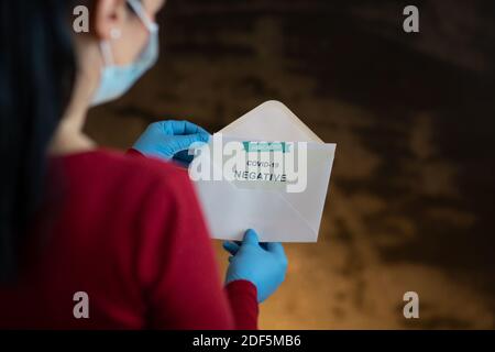 Woman Holding negative Antigen Detection Test per Covid-19. Vista posteriore di Donna indossare maschera e guanti tirare certificato medico con Coron negativo Foto Stock