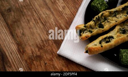 Rollini con brynza e spinaci su un piatto nero con fondo ligneo. Quadrati verdi di spinaci essiccati su un piatto Foto Stock
