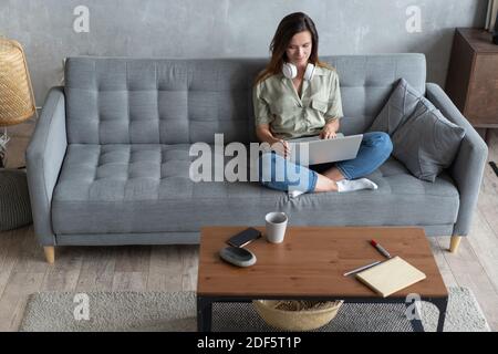 Giovane donna che fa lavoro di ricerca per la sua attività. Donna sorridente seduta sul divano che naviga online sito di shopping Foto Stock