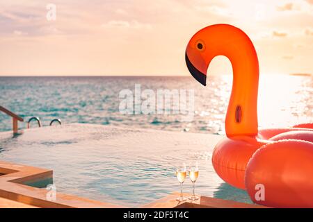 Lussuosa piscina a sfioro. Tramonto vacanza viaggio sfondo vacanza con divertente flamingo giocattolo galleggiante header uno champagne bicchieri come coppia romantica Foto Stock