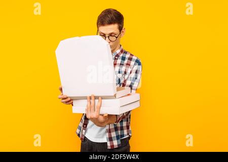 un uomo tiene una scatola di pizza su uno sfondo giallo, un uomo guarda in una scatola di pizza Foto Stock