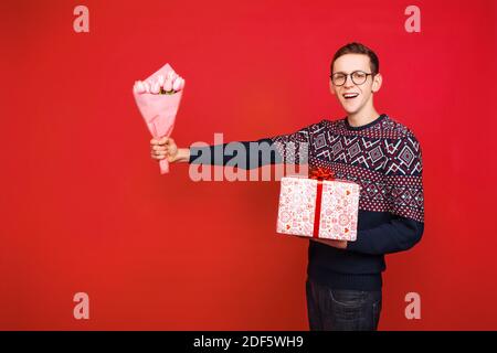 Un uomo in bicchieri contiene un regalo e tiene fuori un mazzo di fiori Foto Stock