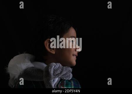 Primo piano ritratto di indiano carino bruna poco allegro Tamil baby boy che indossa un abito casual e un silenziatore di pelliccia in un sfondo nero Foto Stock