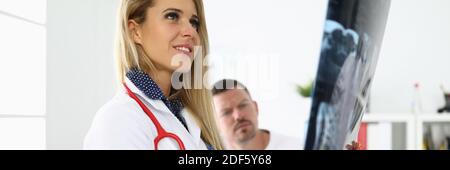 La dottoressa sta tenendo un radiografia accanto al paziente seduto. Foto Stock
