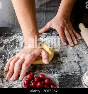 Le mani dell'uomo impastano l'impasto per la preparazione di strudel di ciliegio. Ingredienti da forno. Vispette fatte in casa Foto Stock