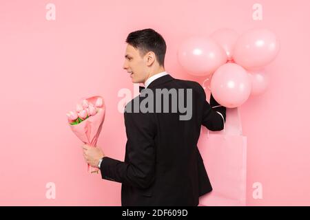 uomo elegante, in costume, con un mazzo di fiori e palloncini, su sfondo rosa Foto Stock