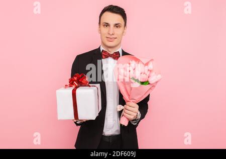 uomo elegante, in costume, con bouquet di fiori, e una confezione regalo, su fondo rosa Foto Stock