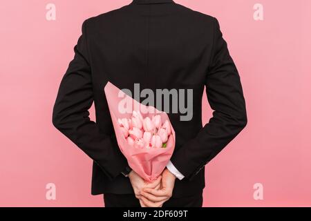 Un uomo tiene dietro la schiena un bouquet di tulipani, una sorpresa per una donna, su sfondo rosa, il concetto di amore e relazioni Foto Stock
