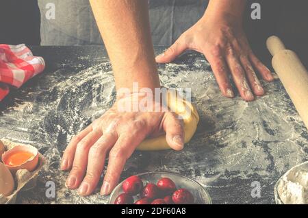 Le mani dell'uomo impastano l'impasto per la preparazione di strudel di ciliegio. Ingredienti da forno. Vispette fatte in casa Foto Stock