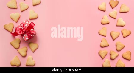 Banner di biscotti fatti in casa a forma di cuore e regalo su sfondo rosa. Vista dall'alto. Biglietto d'auguri per il giorno di San Valentino con spazio per la copia. Disposizione piatta. Foto Stock