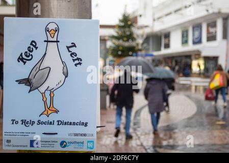 High Street, Southend on Sea, Essex, Regno Unito. 3 dicembre 2020. Nonostante il freddo e il clima umido sleety acquirenti sono fuori in High Street a Southend on Sea, con i segni dell'artista locale Sarah Judd che chiede alla gente di rimanere a sinistra per aiutare la distanza sociale. Persone con ombrelloni Foto Stock