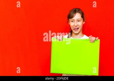 Giovane adolescente caucasica auto-soddisfatto che tiene foglio di carta bianco su sfondo rosso dello studio. Foto Stock