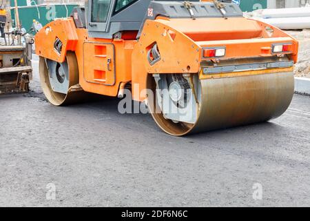 Costruzione di una nuova strada. Un grande rullo vibrante per la circolazione su strada abbinato a un'asfaltatrice che stesa e compatta l'asfalto caldo sulla nuova strada. Foto Stock