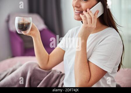 Donna adulta che parla al telefono e che ha un caffè bere Foto Stock