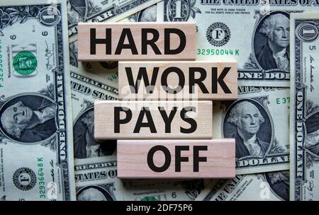 Il duro lavoro paga fuori il simbolo. Pila di blocchi di legno con le parole 'lavoro duro paga fuori'. Bella sfondo dalle fatture del dollaro. Affari e duro lavoro pagano o Foto Stock