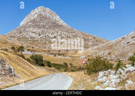 Paesaggio con strada di montagna e picco Camicia ripidi pendii rocciosi, sparati in luce intensa vicino al passo di Capo la Serra, l'Aquila, Abruzzo, Italia Foto Stock