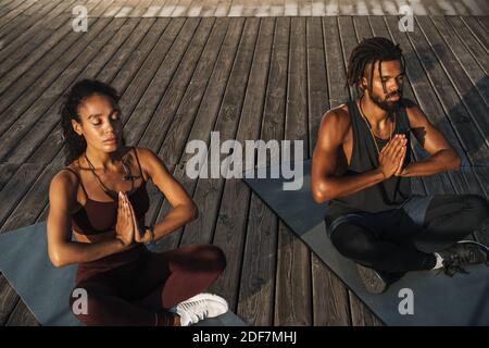 Calma afro coppia americana facendo esercizi di yoga all'aperto, seduto su un tappetino fitness Foto Stock