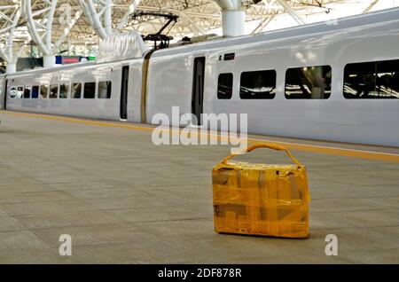 Abbandonato self made valigia di cartone posa sulla stazione ferroviaria quay pavimento della piattaforma in Cina. Guardando il sospetto, nessuno attorno, treno veloce in background. Foto Stock