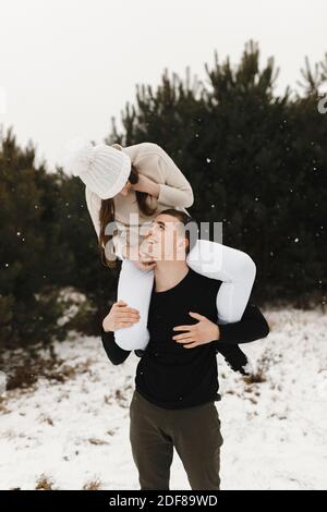 Uomo sorridente che tiene la donna sulle spalle in inverno. Inverno divertente tempo. Amore, rapporto, vacanze invernali. Idee di foto di coppia di inverno Foto Stock