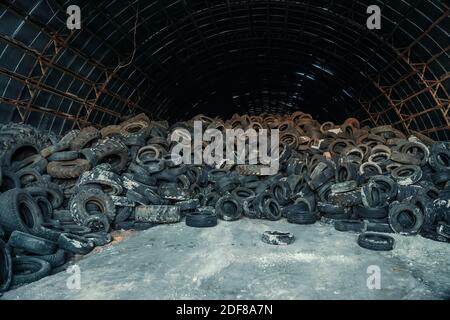 Grande pila di vecchi pneumatici usati e camion in hangar abbandonato. Foto Stock