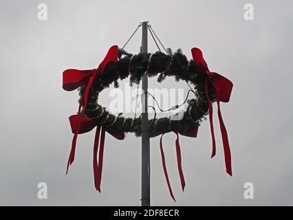 Corona di Natale con nastri rossi su un palo. Cielo grigio come sfondo. Corona dell'avvento Foto Stock