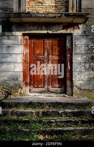 Portico di un vecchio palazzo con una scala in pietra e. una porta rossa Foto Stock