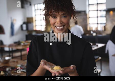 Ritratto di una chef afro-americana che tiene in mano ravioli alla cucina del ristorante Foto Stock