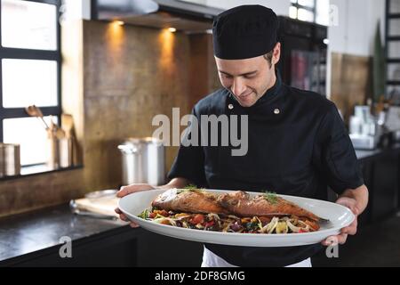 Chef caucasico maschile con un piatto di pesce arrosto alla cucina del ristorante Foto Stock