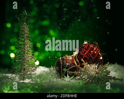 Ornamento di Natale rosso e un albero di Natale lucido su sfondo verde con neve caduta in ambienti bui moody. Vacanze invernali artistiche, anno nuovo con Foto Stock