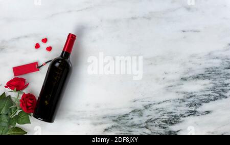 Buon giorno di San Valentino con graziosi fiori di rosa rossa e inaperti bottiglia di vino rosso su fondo in marmo naturale Foto Stock