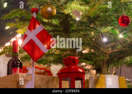 Bellissimo albero di Natale con bandiera danese, candeliere scandinavo, ornamenti e luci, lanterna e bottiglia di vino in una scatola di legno, sfondo Foto Stock